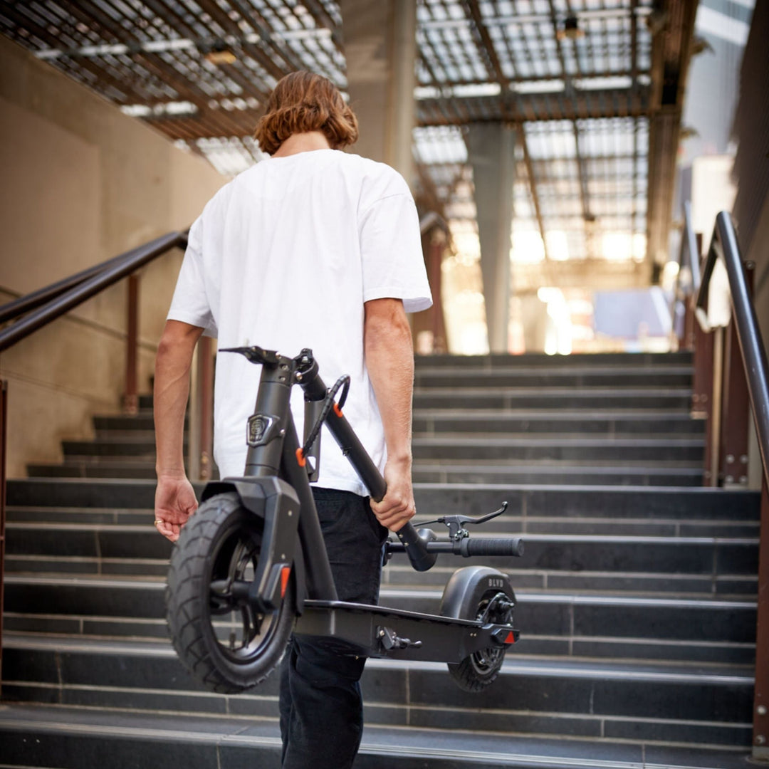 young man carrying a blvd elite electric scooter up stairs
