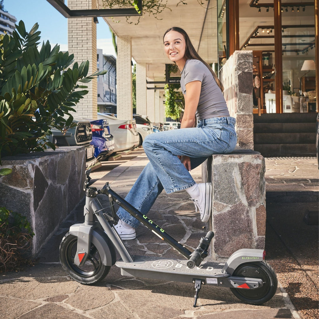 female adult in street clothes sitting next to a folded down blvd urban plus electric scooter